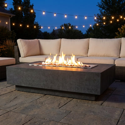 Elementi Hampton fire pit table with flames lit on an evening patio in front of an outdoor sofa