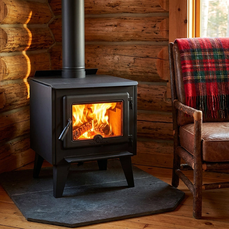 True North black wood stove with fire burning on a slate hearth pad in a log cabin