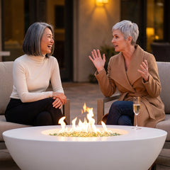 Two friends beside the white AFD Calais Oval fire table at blue hour