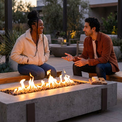 Two friends around the shin-height AFD Iron Saddle Long fire table at dusk