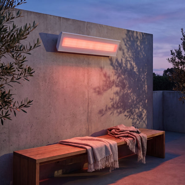 Bromic Platinum Smart-Heat Electric 3400W white panel glowing over a courtyard bench at dusk