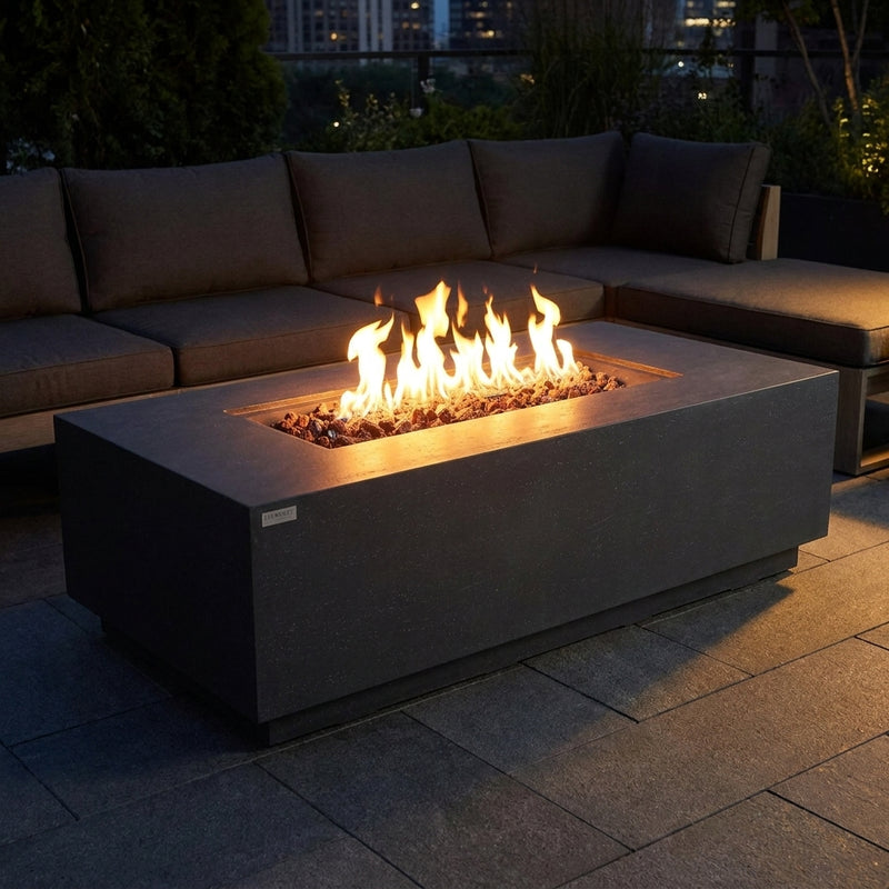 Dark gray Elementi Andes fire pit table with tall flames over lava rock on a modern patio at night