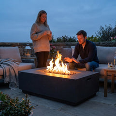 Two people beside the 22-inch-tall Elementi Andes fire pit table at dusk