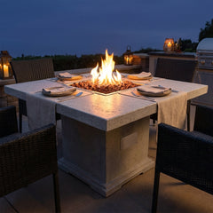 Elementi Birmingham dining-height fire pit table with flames over lava rock set for dinner at dusk