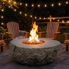 Elementi Boulder natural rock-look fire pit with flames lit between Adirondack chairs at night