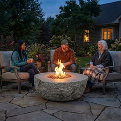 Three friends laughing around the 16-inch-tall Elementi Boulder fire pit at dusk