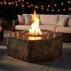Elementi Columbia basalt boulder fire pit table with flames lit on an evening patio