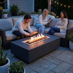 Friends seated around the 17-inch-tall Elementi Granville fire pit table at dusk, one warming their hands over the flames