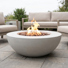 Light gray Elementi Lunar Bowl fire pit table with flames lit on a stone patio in daylight