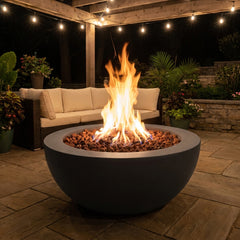 Elementi Lunar Bowl fire pit table with flames lit on an evening patio under string lights