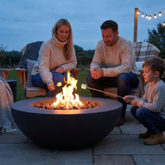 Family roasting marshmallows around the 16-inch-tall Elementi Lunar Bowl fire pit at dusk