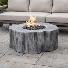 Classic Gray Elementi Manchester tree-stump fire pit table with flames lit on a stone patio in daylight