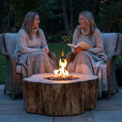 Two friends with blankets beside the 17-inch-tall Elementi Manchester stump fire table at dusk