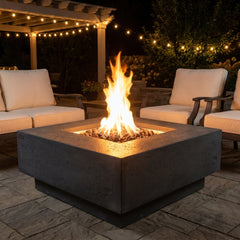 Elementi Manhattan square fire pit table with flames lit on an evening patio under string lights