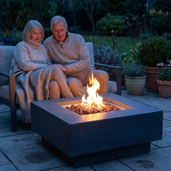 Couple relaxing beside the 16-inch-tall Elementi Manhattan square fire pit table at dusk