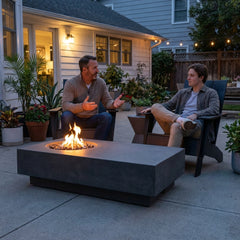 Father and son talking beside the 14-inch-tall Elementi Metropolis fire table at dusk