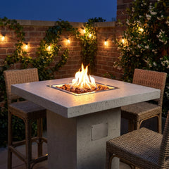Elementi Montreal light gray bar-height fire pit table with flames over lava rock on a bistro patio at dusk