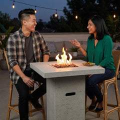 Two friends laughing at the bar-height Elementi Montreal fire pit table at dusk