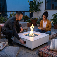 Two people beside the 14-inch-tall Elementi Plus Annecy square porcelain fire table at dusk