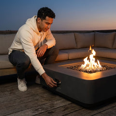 Man crouching to adjust the shin-height Elementi Plus Bergamo square fire pit table at dusk