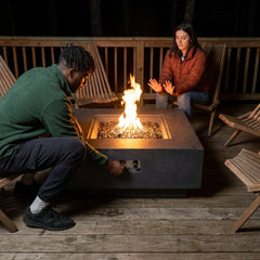 Two people warming up beside the seat-height Elementi Plus Bergen square fire table at night