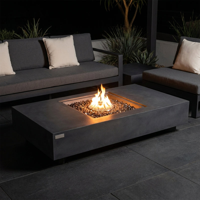 Elementi Plus Cannes dark charcoal fire table with a square burner recess and bronze fire glass on a modern patio at night