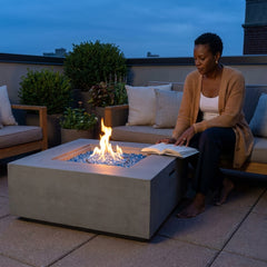 Woman reading beside the shin-height Elementi Plus Capertee sandstone fire pit table at blue hour