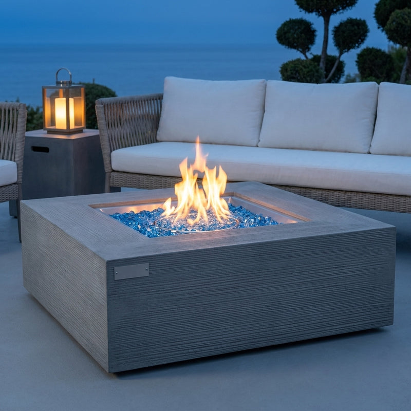 Elementi Plus Capertee space gray sandstone fire pit table with flame over Caribbean blue fire glass at blue hour