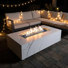 Elementi Plus Carrara marble-look porcelain fire pit table with flames over blue fire glass on an evening patio