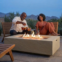 Couple sharing iced tea beside the 15-inch-tall Elementi Plus Colorado sandstone fire table at dusk