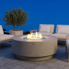 Elementi Plus Colosseo round light gray concrete fire pit table with flame over Caribbean blue fire glass at blue hour