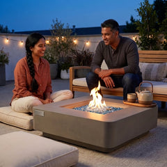 Couple relaxing around the shin-height Elementi Plus Lucerne square fire pit table at blue hour
