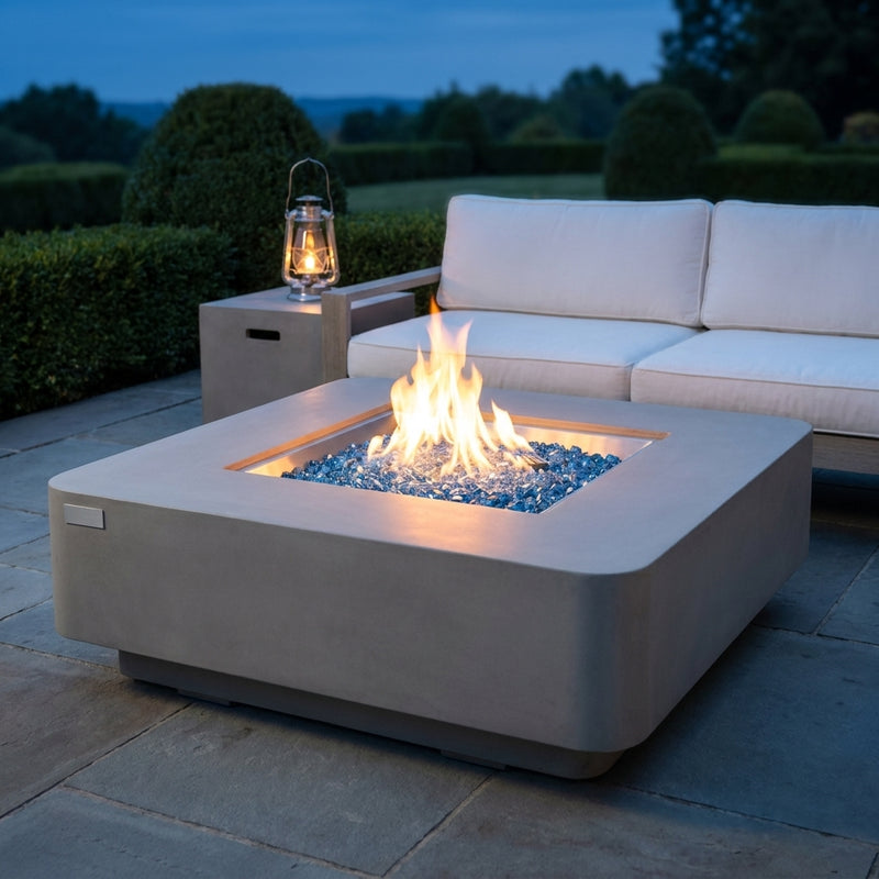 Elementi Plus Lucerne low square light gray concrete fire pit table with flame over Caribbean blue fire glass at blue hour