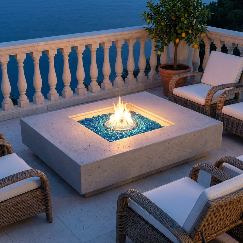 Elementi Plus Monte Carlo light gray fire table with a square burner recess and Caribbean blue fire glass on a Mediterranean terrace at dusk