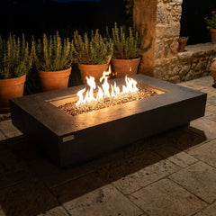 Elementi Plus Positano dark gray sandstone fire table with flames over bronze fire glass at night
