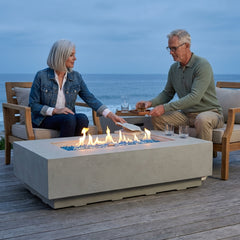 Couple reading and pouring drinks beside the 14-inch-tall Elementi Plus Riviera sandstone fire table at dusk