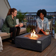 Two friends around the shin-height Elementi Plus Roraima sandstone fire pit table at dusk