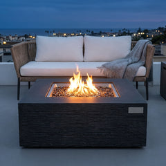 Elementi Plus Roraima slate black sandstone fire pit table with flame over bronze fire glass on a rooftop terrace at dusk