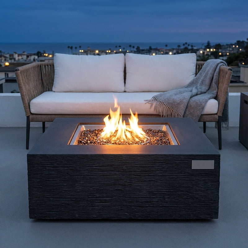 Elementi Plus Roraima slate black sandstone fire pit table with flame over bronze fire glass on a rooftop terrace at dusk