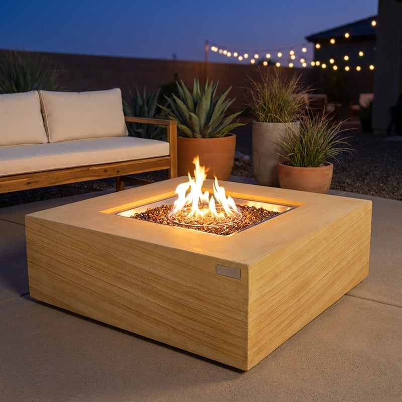 Elementi Plus Uluru sunlight yellow sandstone fire pit table with flame over bronze fire glass in a courtyard at dusk