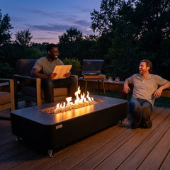 Two friends relaxing beside the 14-inch-tall Elementi Plus Valencia fire table at dusk