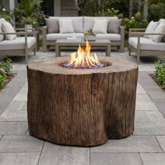 Redwood Elementi Warren stump fire pit table with flames lit on a stone patio in daylight
