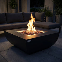 Black Modeno Aurora curved concrete fire pit table with flames over lava rock at night