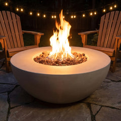 Modeno Roca light gray concrete fire bowl with flames lit between Adirondack chairs at night