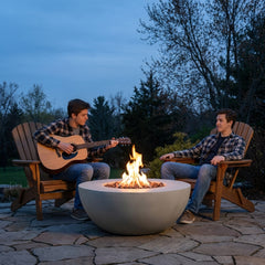 Two friends playing guitar beside the 15-inch-tall Modeno Roca fire bowl at dusk