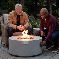 Two friends around the shin-height Modeno Tramore round fire pit table at dusk