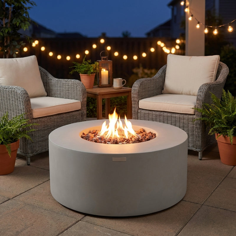 Modeno Tramore round light gray concrete fire pit table with flames over lava rock on a patio at dusk