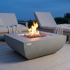 Light gray Modeno Westport curved concrete fire pit table with flames over lava rock at dusk