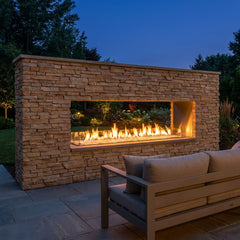 Outdoor Greatroom 72 inch see-through ready-to-finish gas fireplace shown installed in an owner-finished stone wall at dusk
