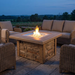 Outdoor Greatroom Sierra Square gas fire pit table lit on a paved patio at dusk